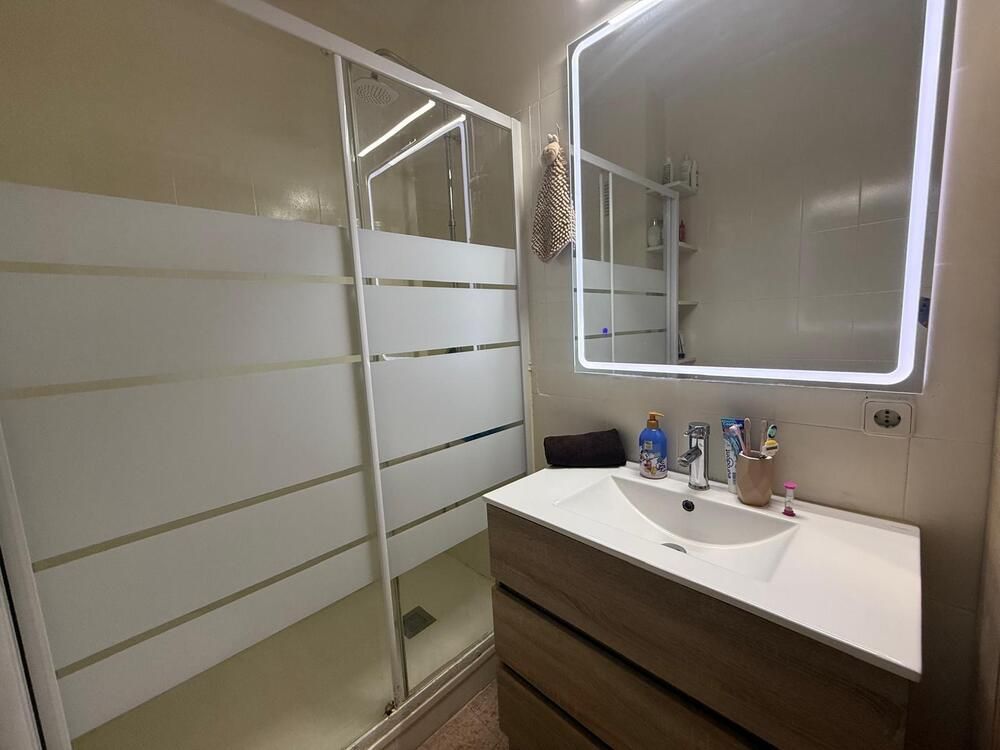 Baño con tocador moderno, espejo y ducha con vidrio esmerilado.