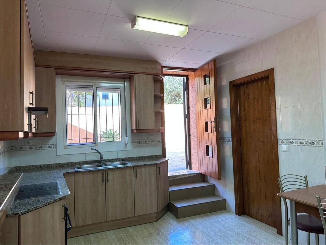 Cocina con armarios de madera, ventana y puerta que da al exterior con escalones.