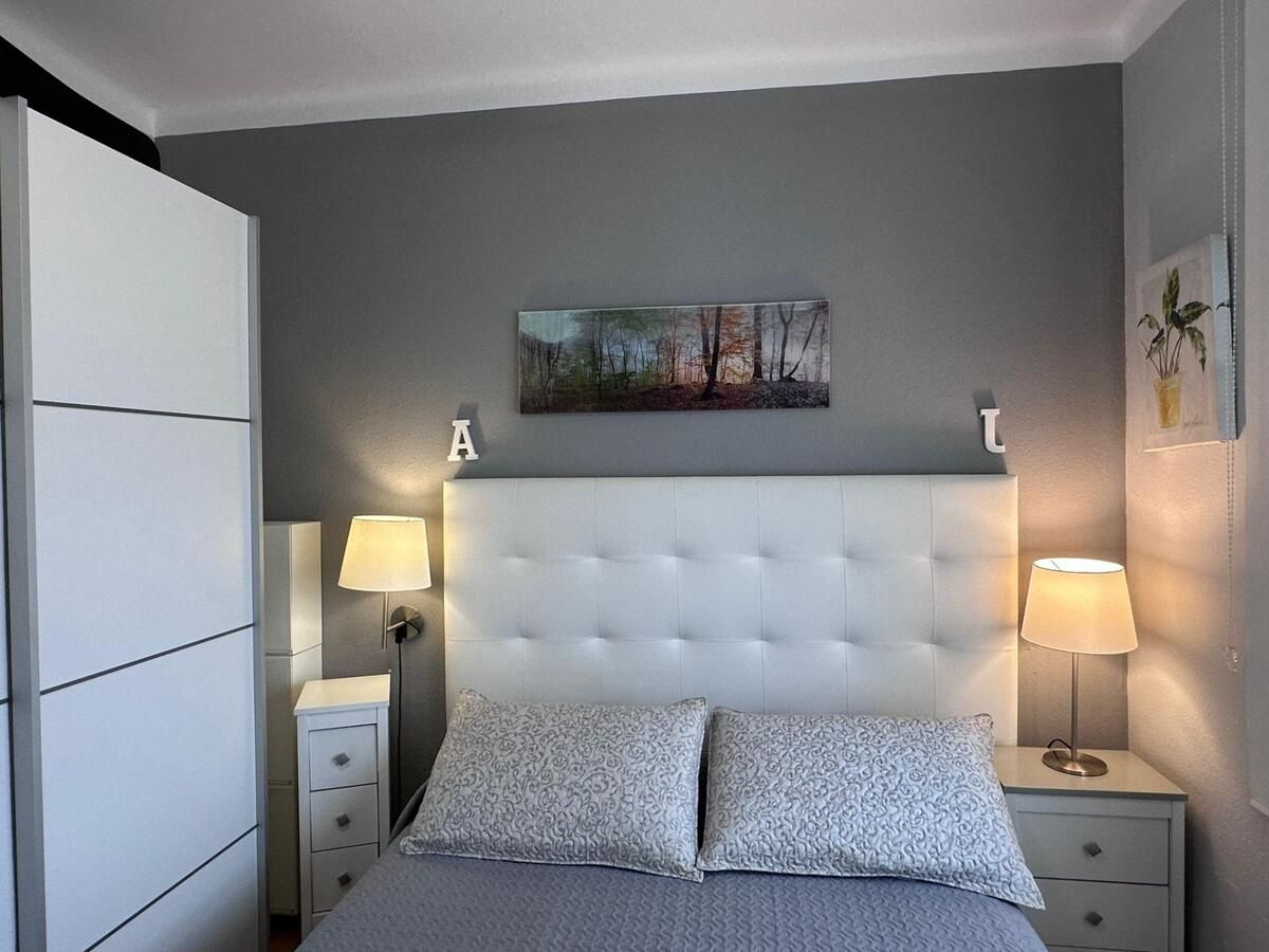 Dormitorio con cama blanca, paredes grises, obras de arte y mesitas de noche con lámparas.