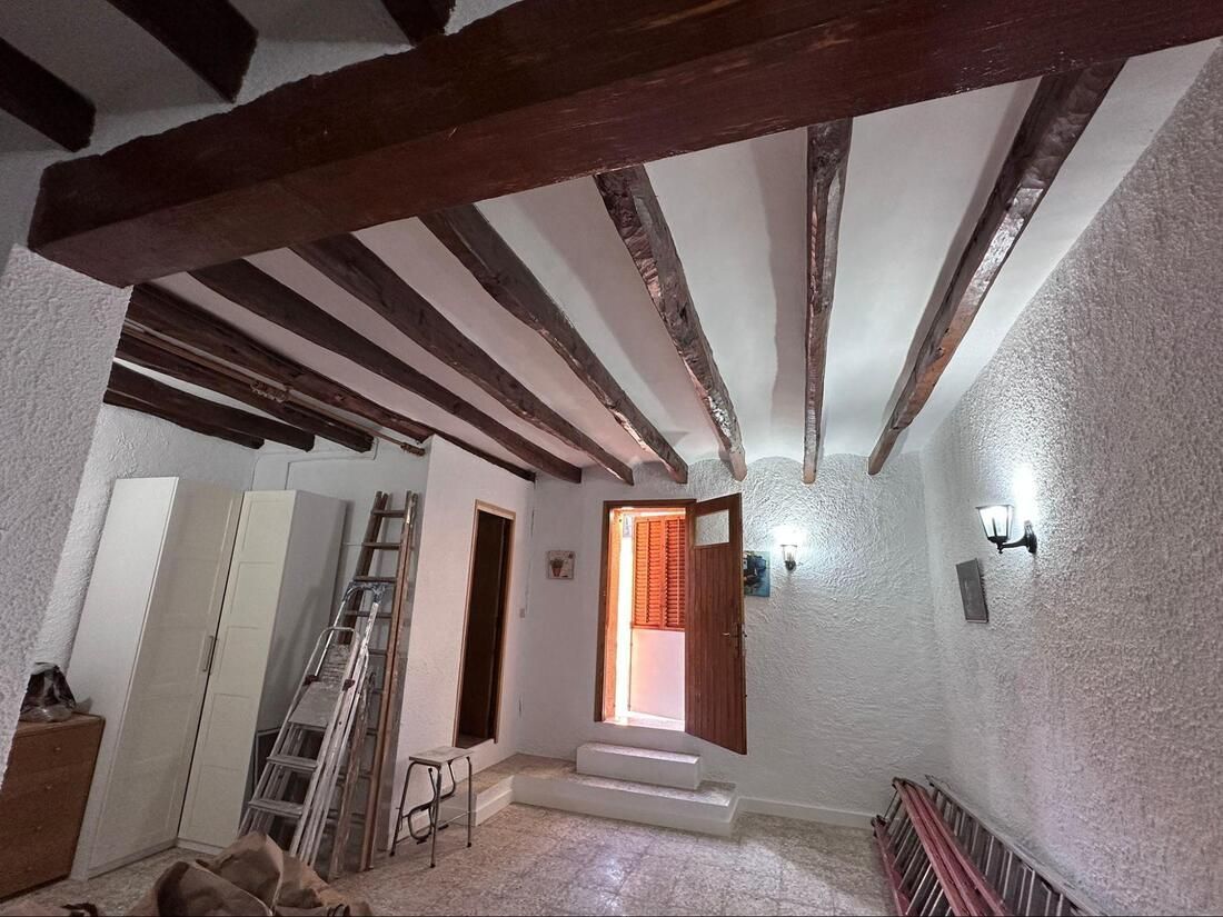 Habitación con vigas de madera a la vista en el techo, paredes blancas texturizadas y puerta de madera abierta.