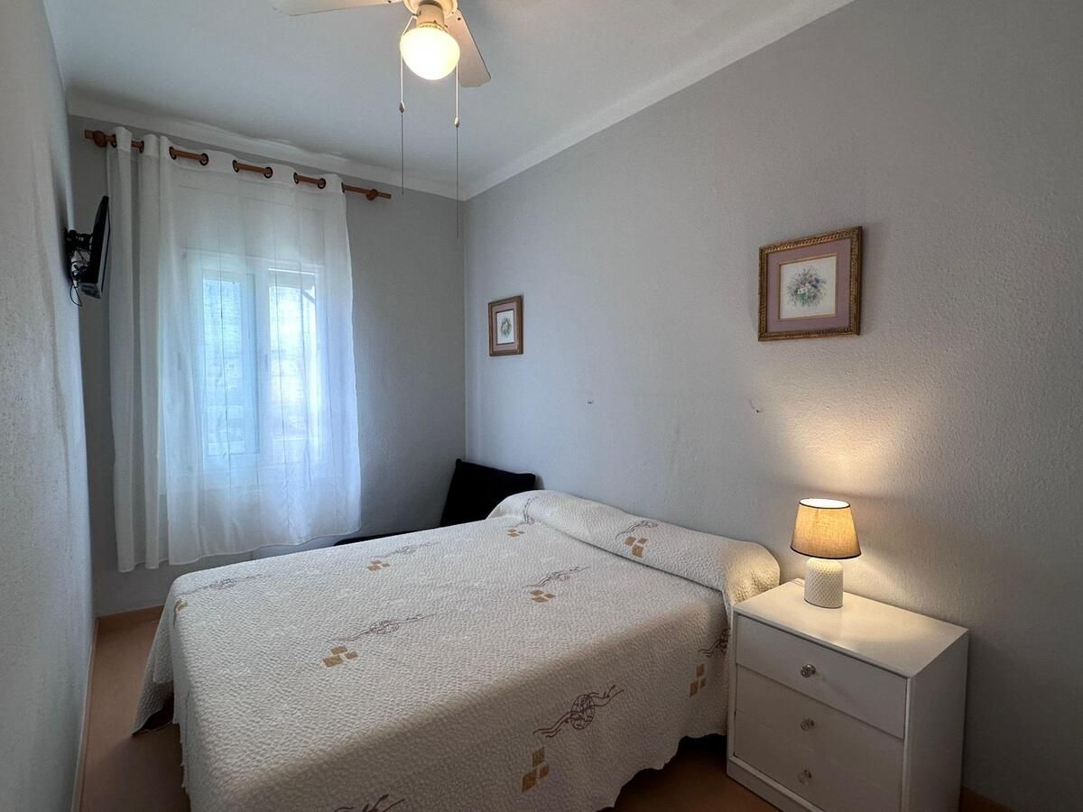 Dormitorio con cama, mesita de noche, ventana y arte enmarcado sobre paredes grises.