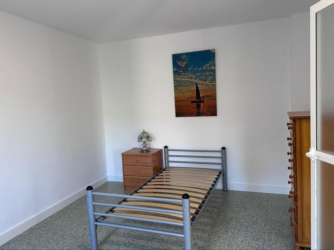 Dormitorio pequeño con una cama individual, cómoda de madera y obras de arte en una pared blanca.