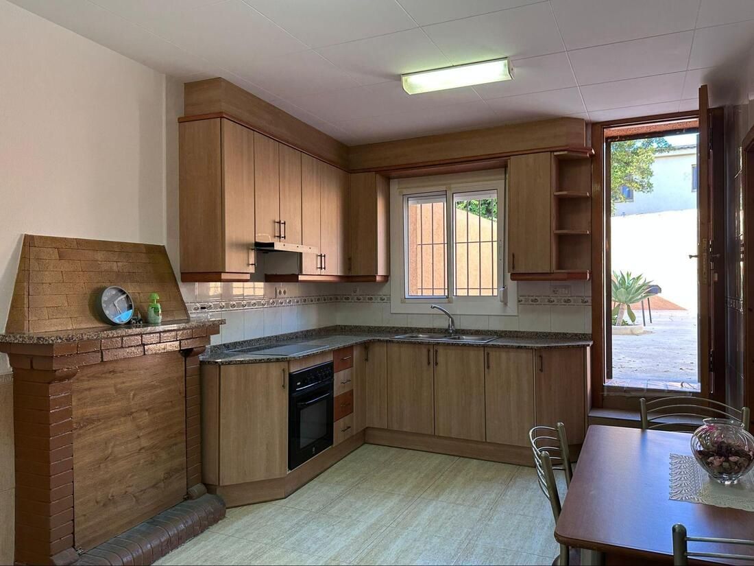 Cocina con armarios de madera, ventana y puerta que da a un espacio exterior. Armarios y suelo de color marrón claro.