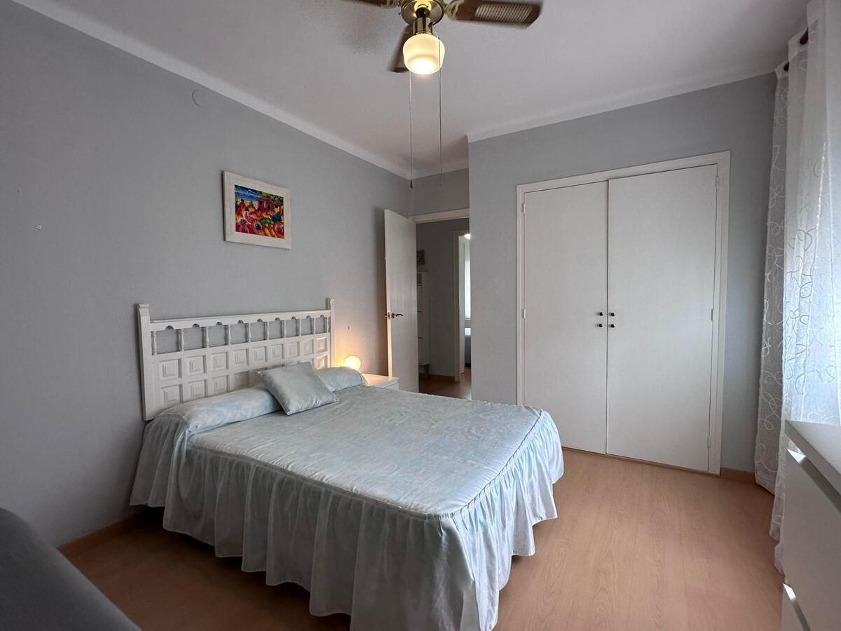 Dormitorio con cama, cabecero blanco y armario; colcha azul, paredes grises, suelo de madera.