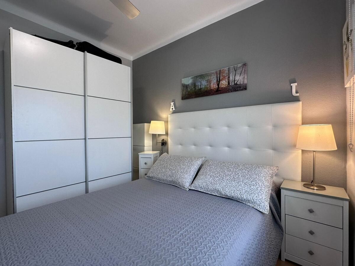 Dormitorio con pared gris, cama blanca, mesitas de noche y armario. Un cuadro cuelga sobre la cama.