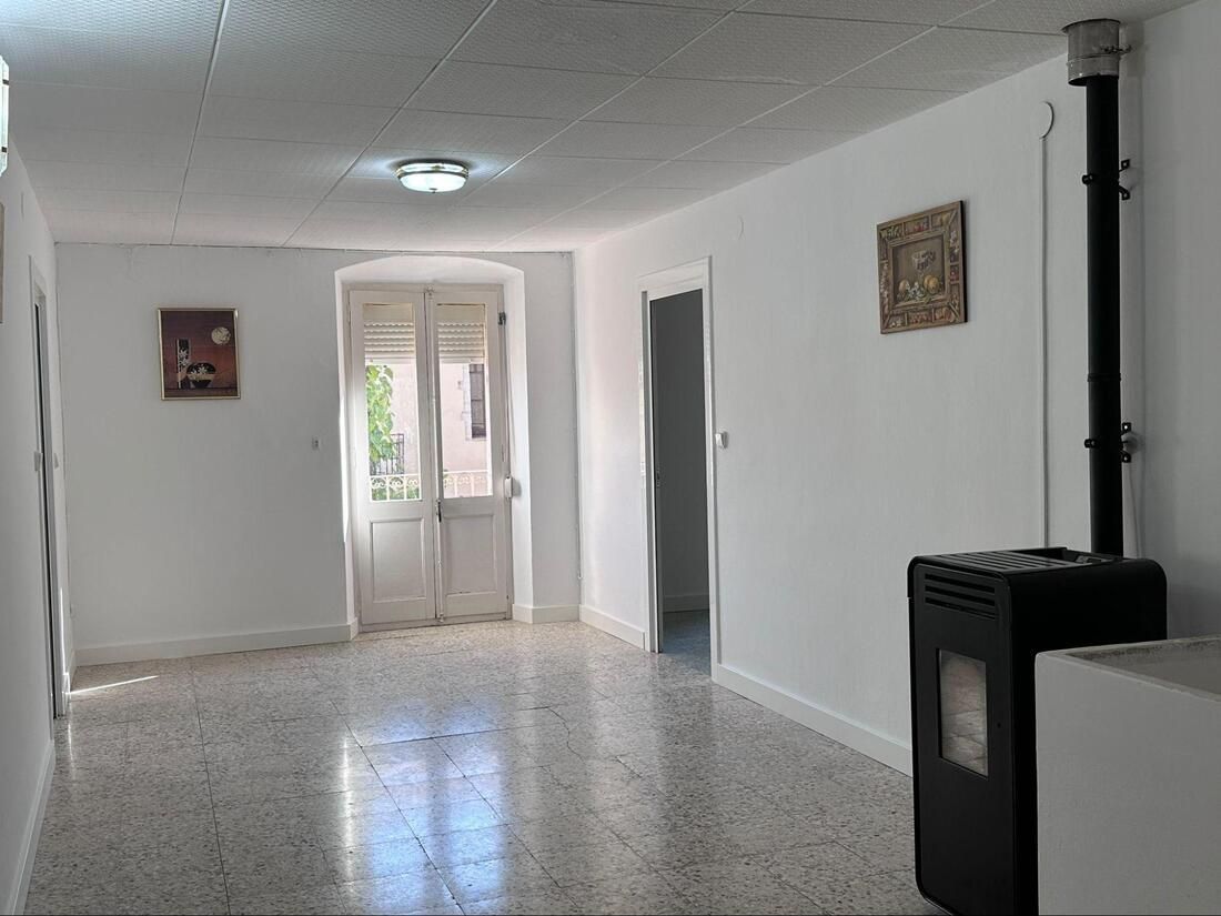 Habitación blanca luminosa con suelo de terrazo, puerta blanca, estufa negra y obras de arte.