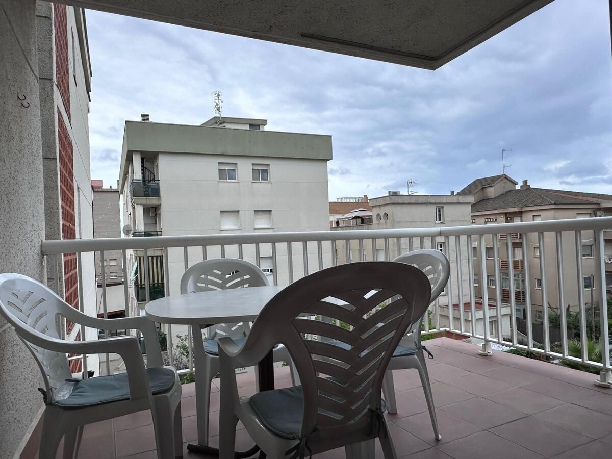 Balcón con mesa y sillas de plástico blanco, con vista a un paisaje urbano nublado.