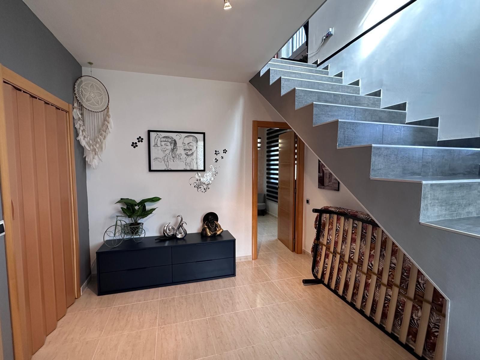 Pasillo con escaleras, puerta de madera, armario negro, obra de arte, atrapasueños y barandilla decorativa.