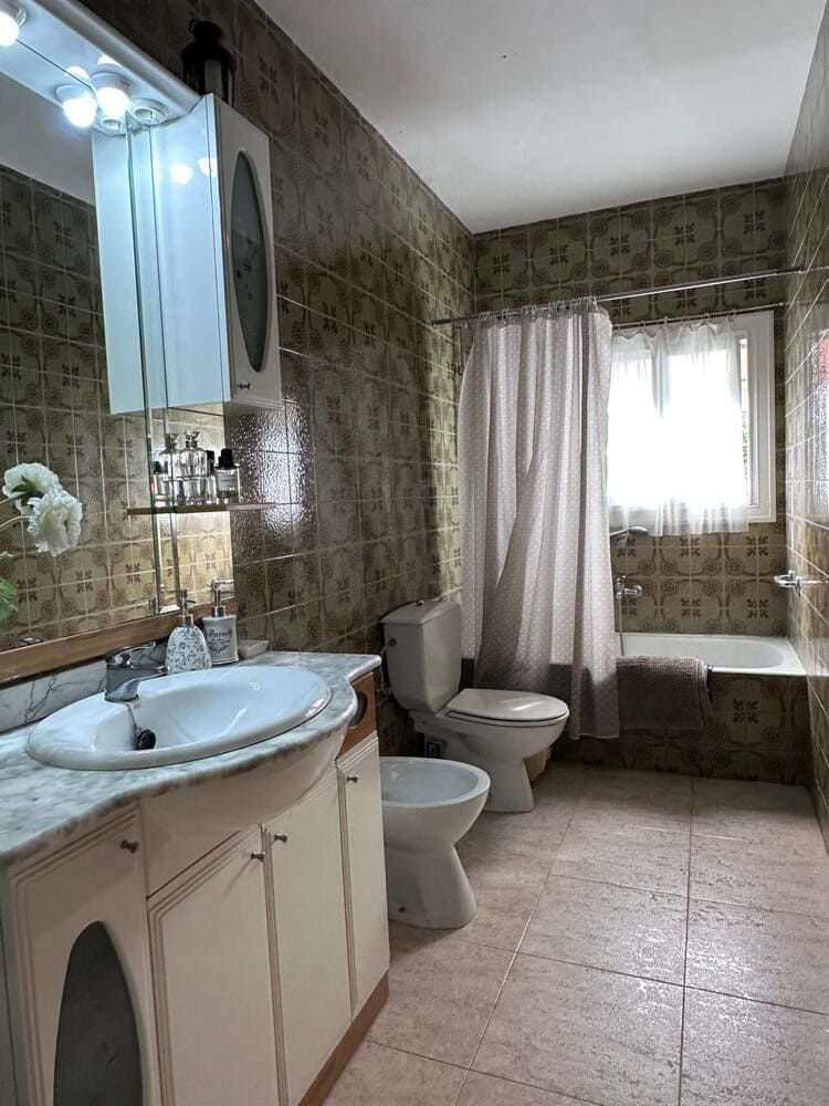 Baño con lavabo, inodoro, bidé y bañera. Paredes y suelo de azulejos verdes. Armarios blancos.