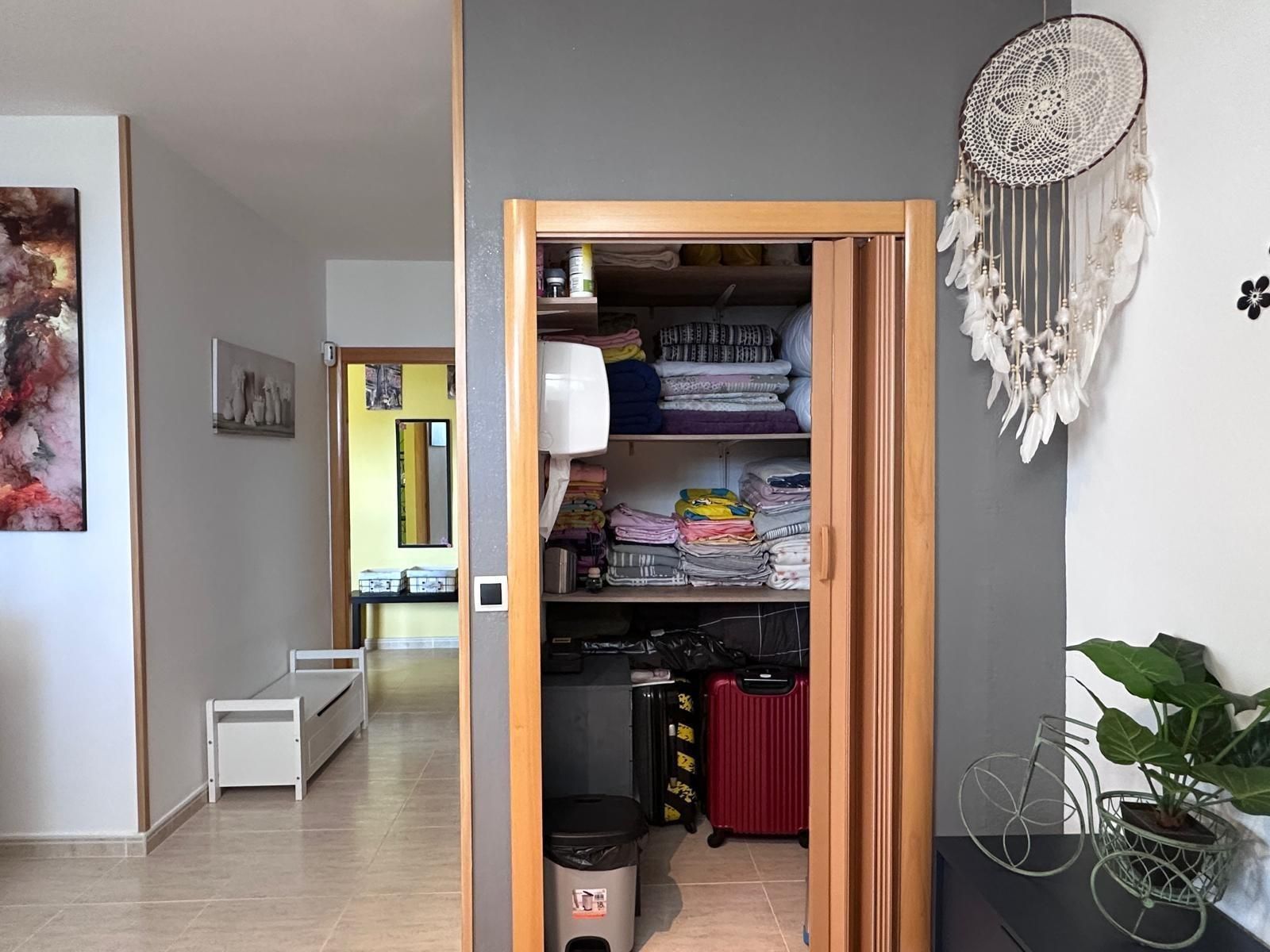 Pasillo con armario abierto; estanterías llenas de objetos, atrapasueños en la pared.