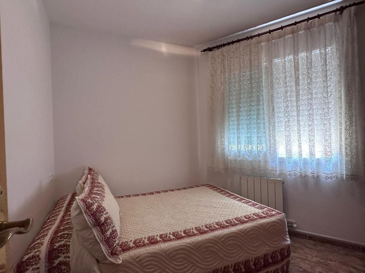 Pequeño dormitorio con una cama individual, una ventana con cortinas y un radiador.