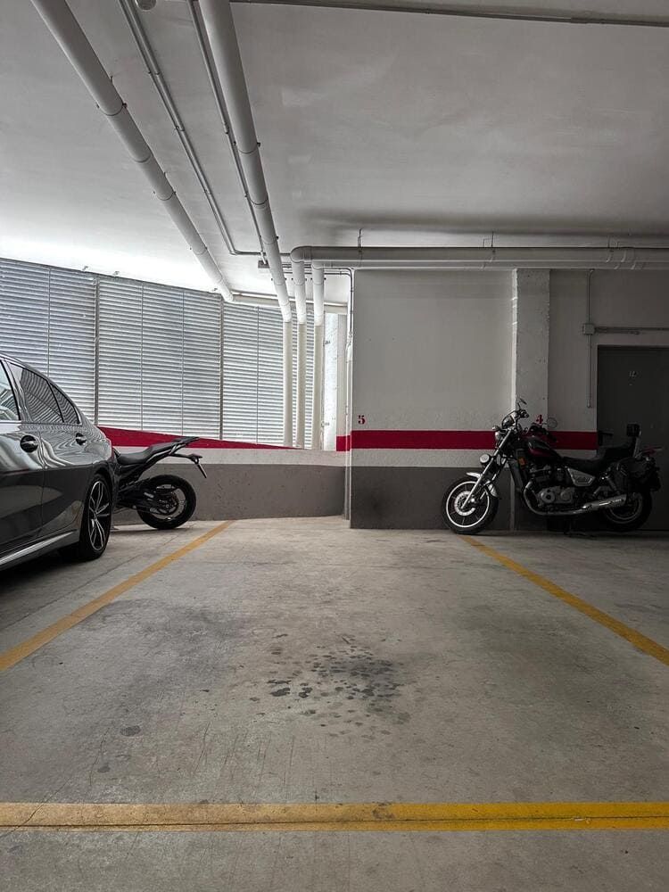 Estacionamiento con un auto, dos motos y líneas amarillas. Pintura gris, blanca y roja.