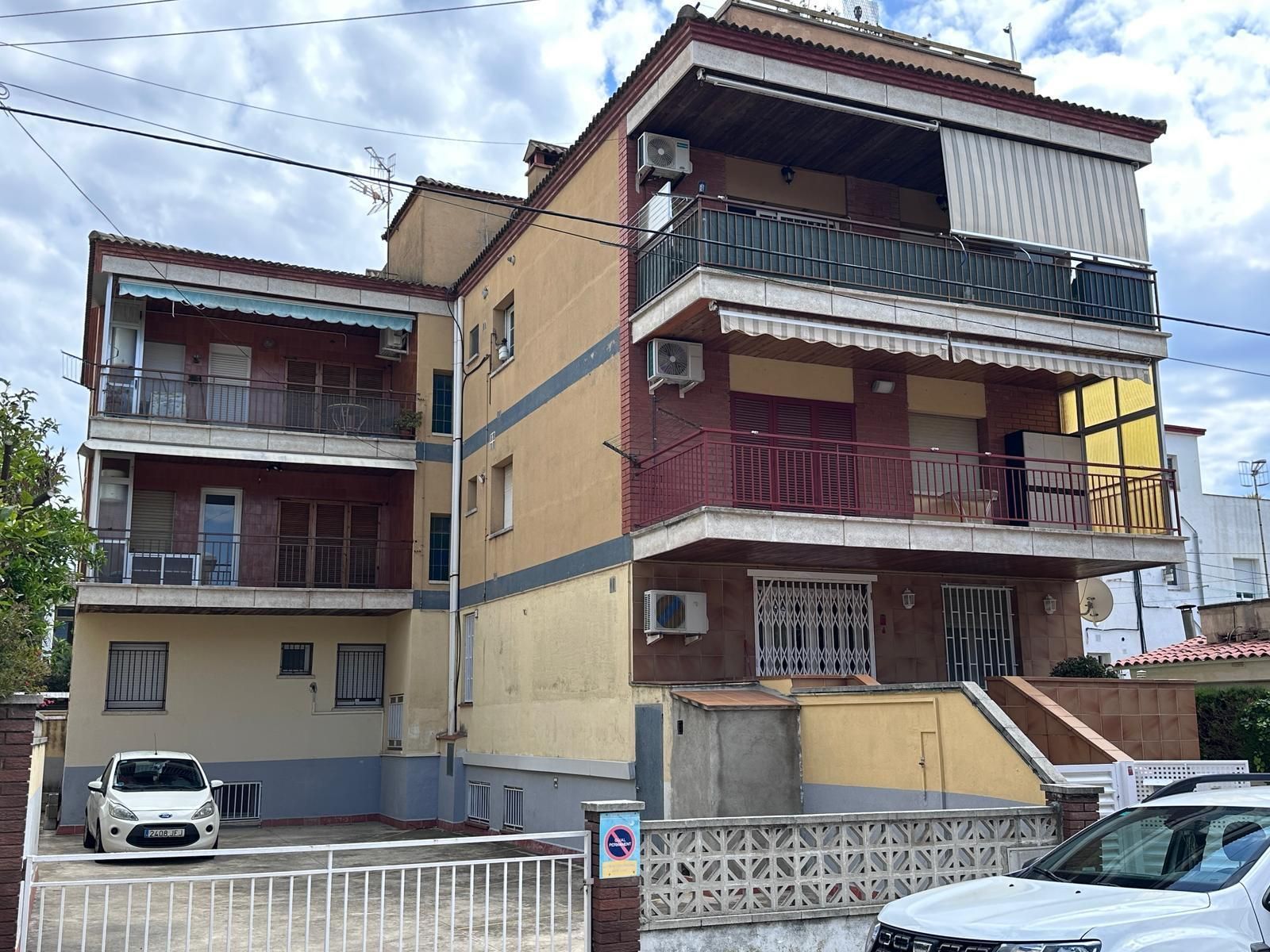 Edificio de apartamentos de varias plantas con balcones y fachada en tonos tostados y granate. Coches aparcados delante.