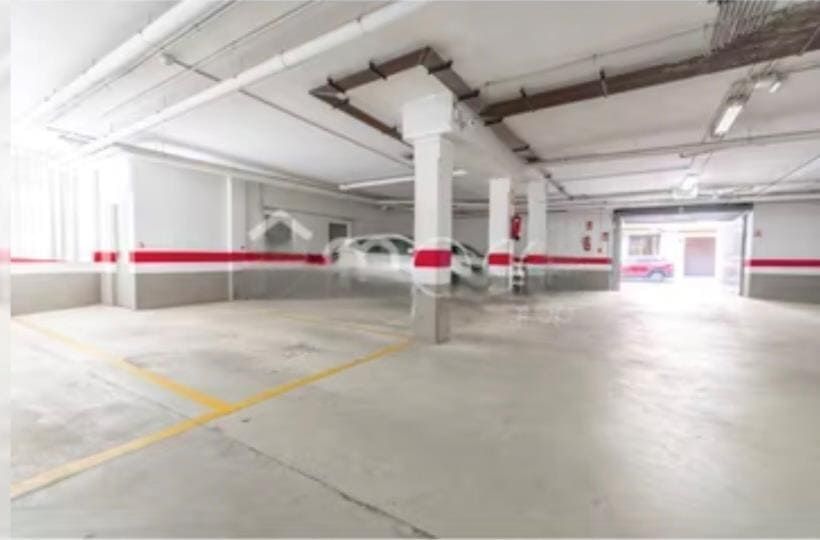 Aparcamiento subterráneo vacío con paredes blancas, rayas rojas y un coche aparcado.