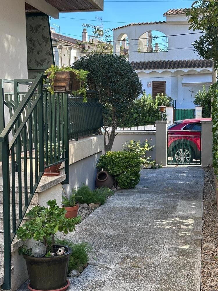 Camino de hormigón que conduce a un coche rojo aparcado cerca de un edificio blanco con ventanas en arco.