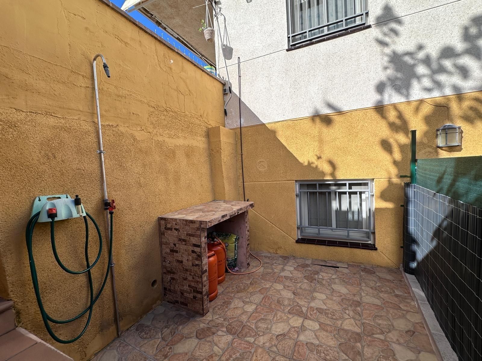 Patio exterior con paredes amarillas, suelo de baldosas, manguera y mostrador de almacenaje.