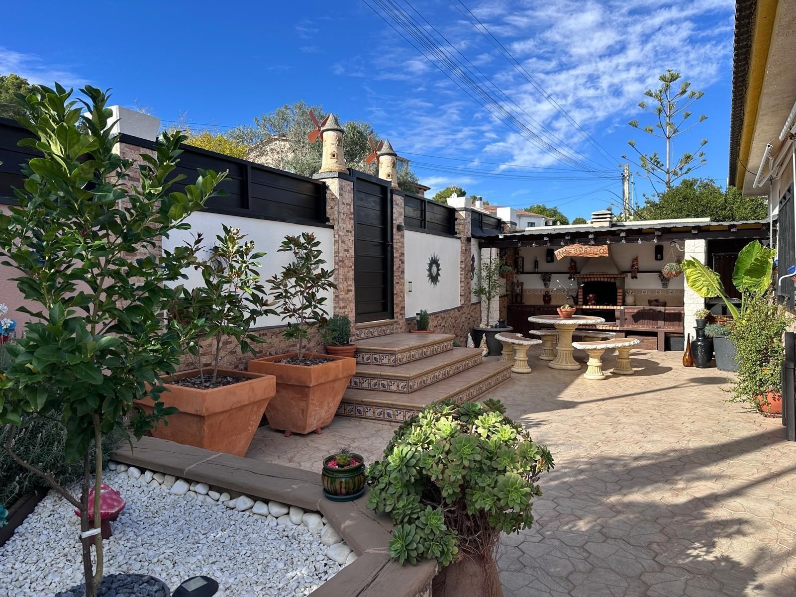 Patio trasero con pavimento de piedra, zona de barbacoa, plantas en macetas y montañas a lo lejos.