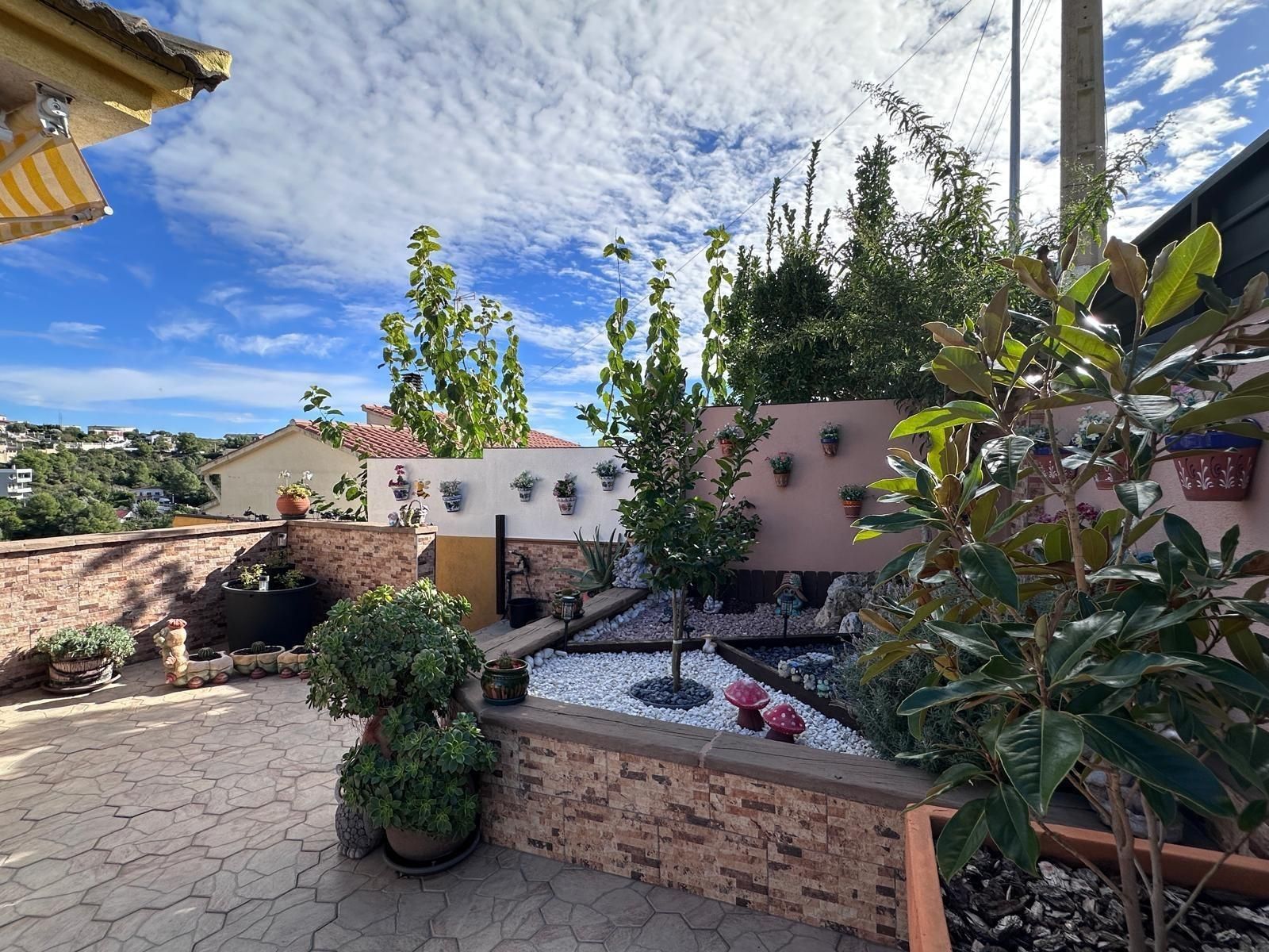 Jardín en terrazas con estanque, plantas y una pared de ladrillos bajo un cielo azul.
