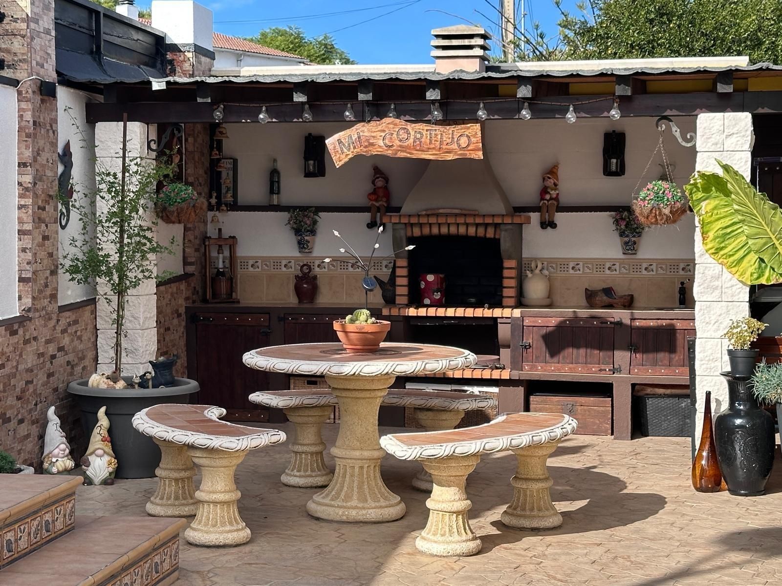 Comedor al aire libre con barbacoa de obra, mesa de piedra y bancos.