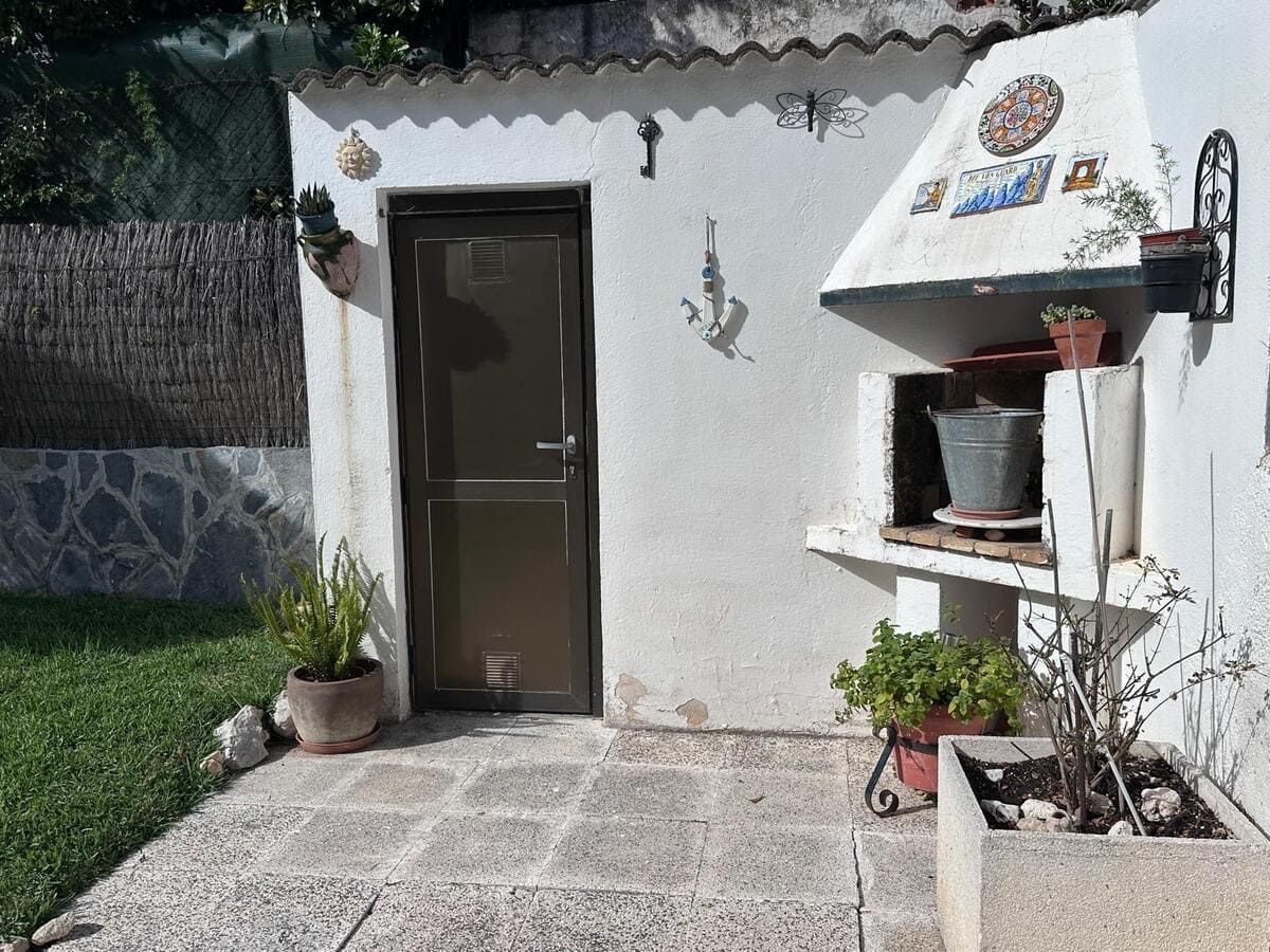 Un patio trasero con puerta, parrilla y plantas en macetas contra una pared de estuco blanco.