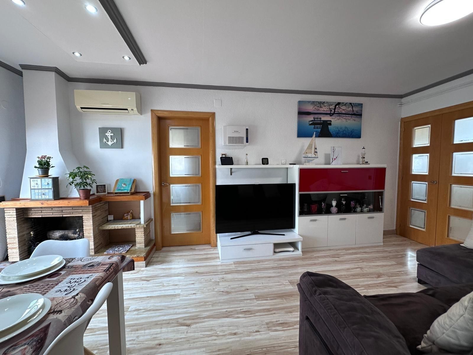 Sala de estar con chimenea, TV y mueble bar. Suelos de color claro, puertas de madera y sofá.