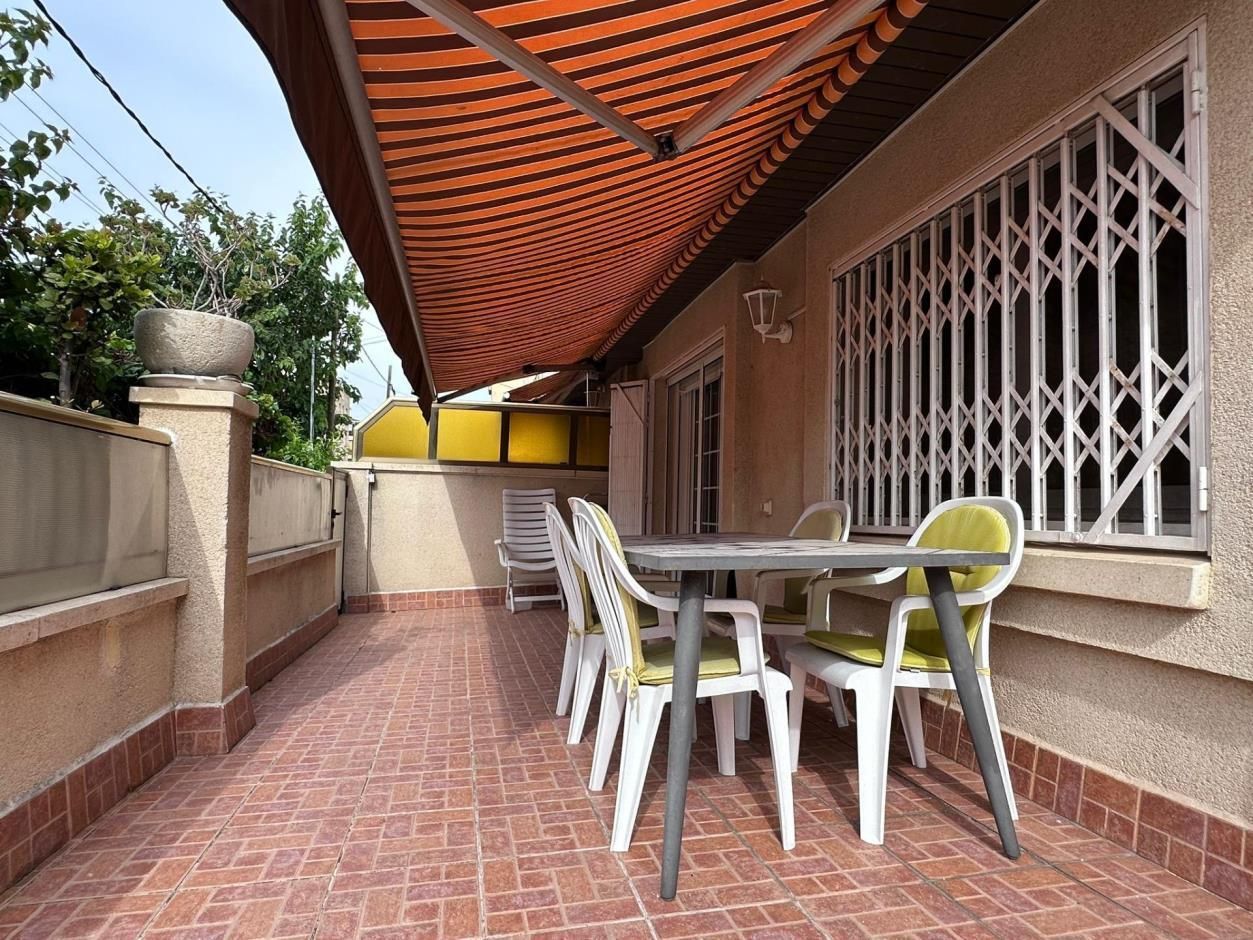 Patio con mesa, sillas y toldo. Suelo y pared de baldosas rojas y rejas de seguridad blancas.