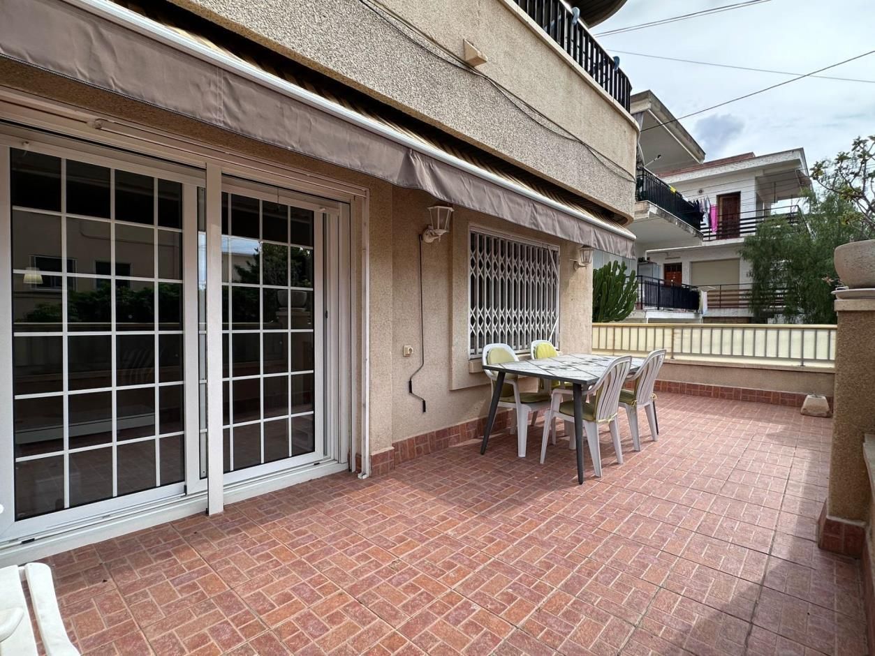 Terraza con mesa y sillas frente a edificio con grandes ventanales y toldo.
