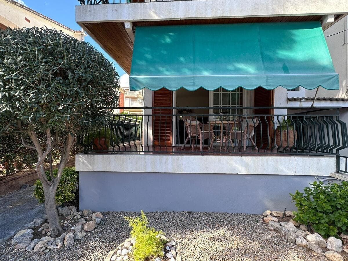 Vista exterior de un balcón con toldo turquesa, muebles de exterior y un árbol.