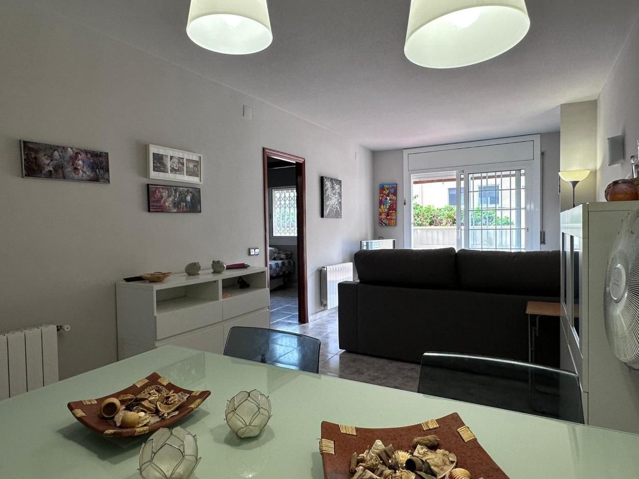 Sala de estar con mesa de comedor, sofá gris y salida a un pasillo y balcón.