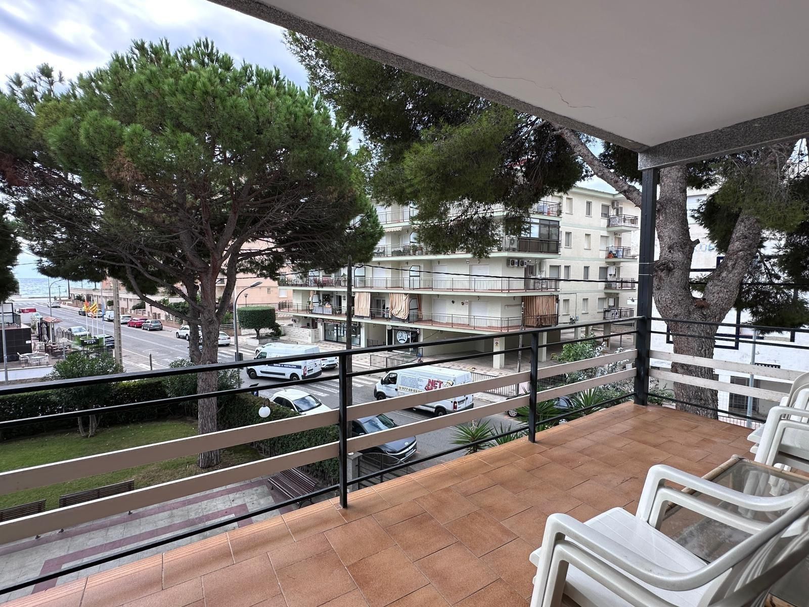 Balcón con sillas blancas con vista a una calle, edificios y un vistazo al mar.