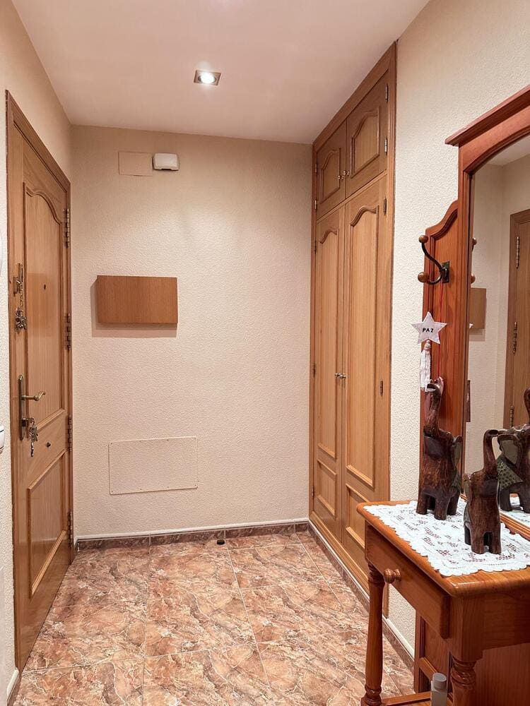 Recibidor con puertas de madera clara, armarios empotrados y consola con espejo, suelo en tonos marrón y tostado.