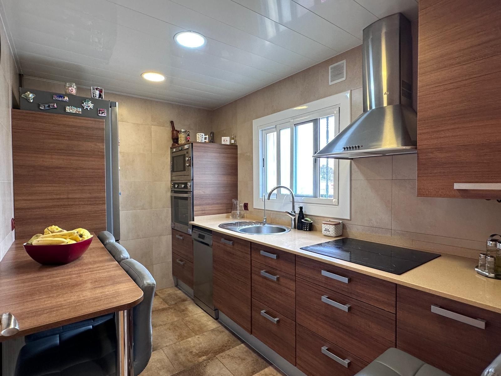Pequeña cocina con gabinetes de madera, electrodomésticos de acero inoxidable y mesa de comedor.