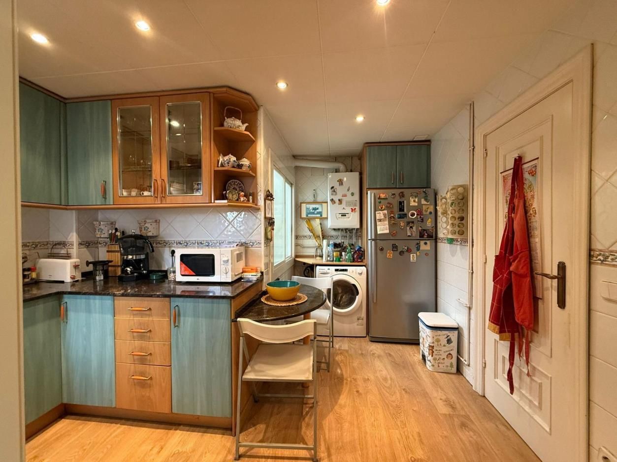Cocina con gabinetes de color verde azulado y madera, electrodomésticos, pequeño comedor.