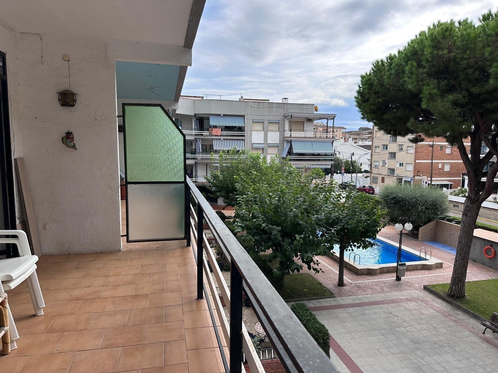 Vista desde el balcón de una piscina y edificios. Se ven árboles y un cielo nublado.