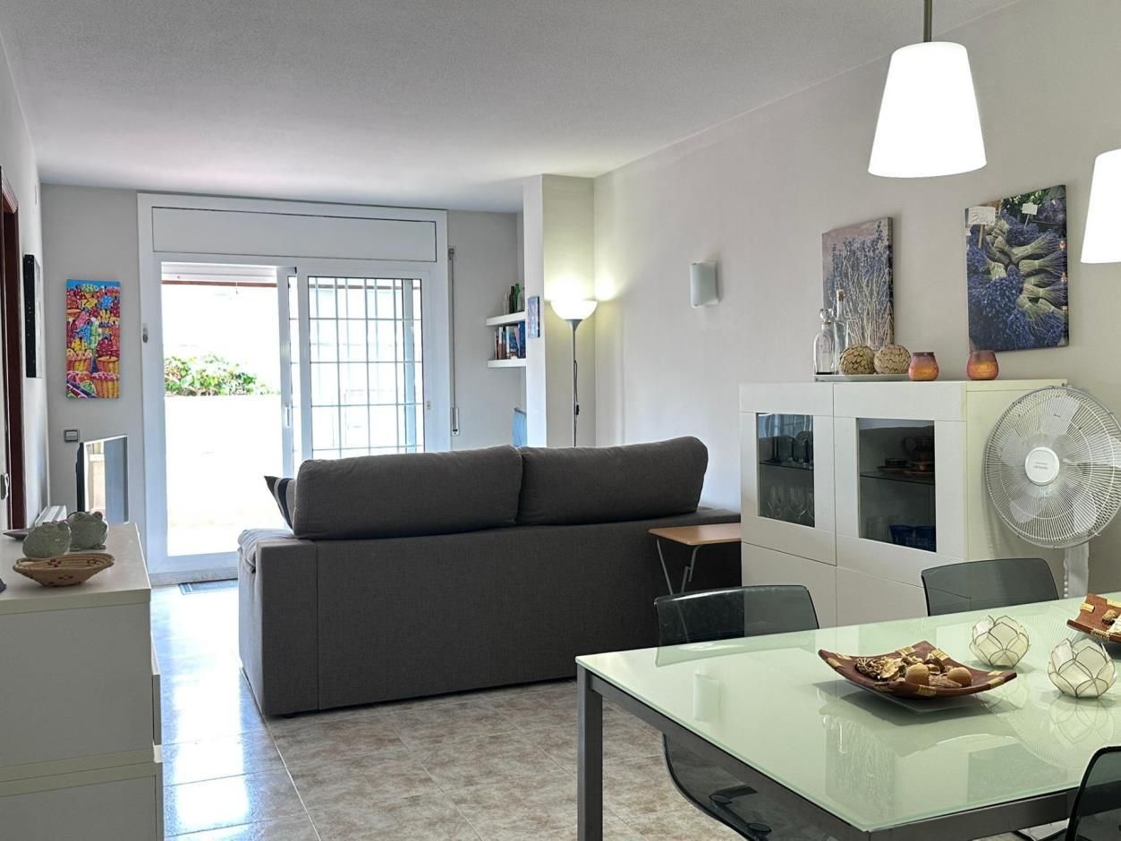 Sala de estar: sofá gris, gabinetes blancos, arte, mesa con sillas y puerta al exterior.