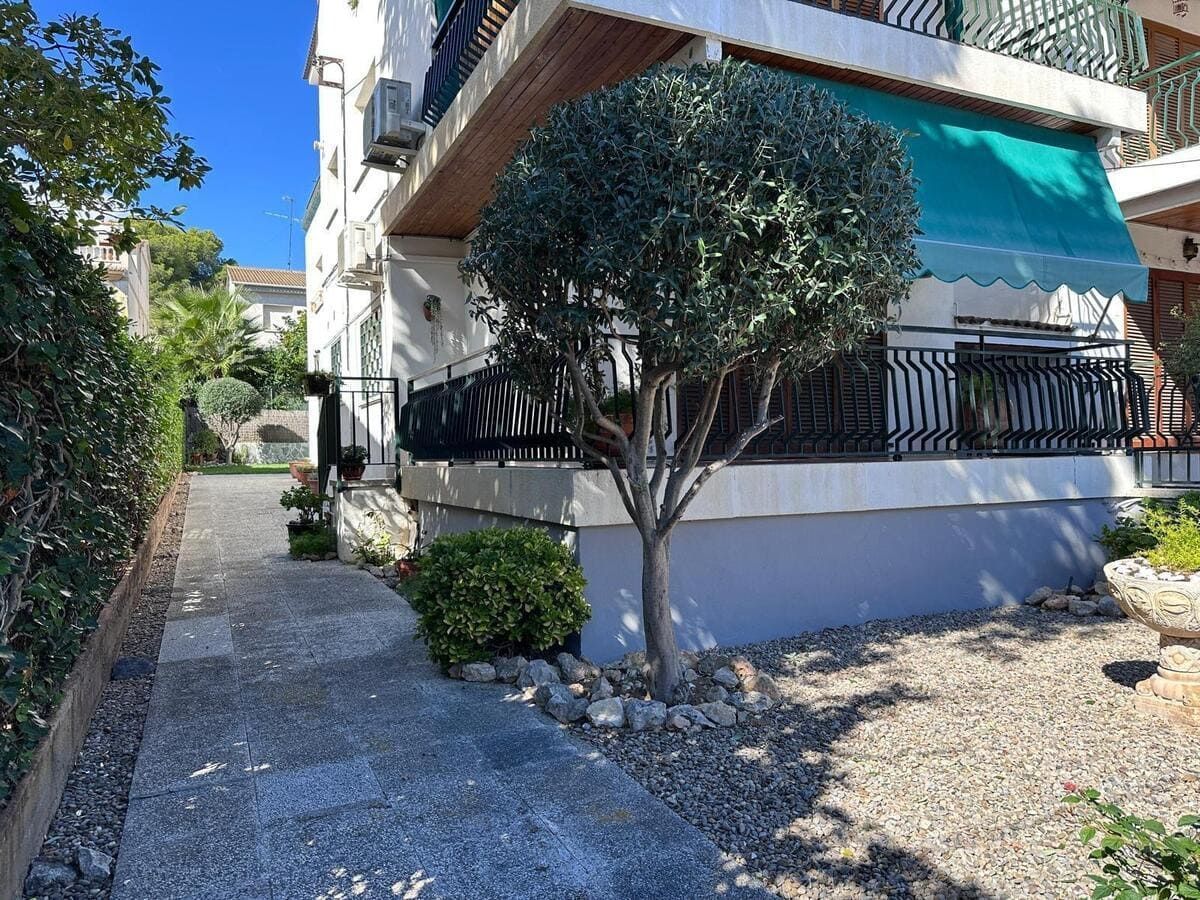 Exterior del edificio con pequeño árbol y paisaje de guijarros, camino a la izquierda, cielo azul.