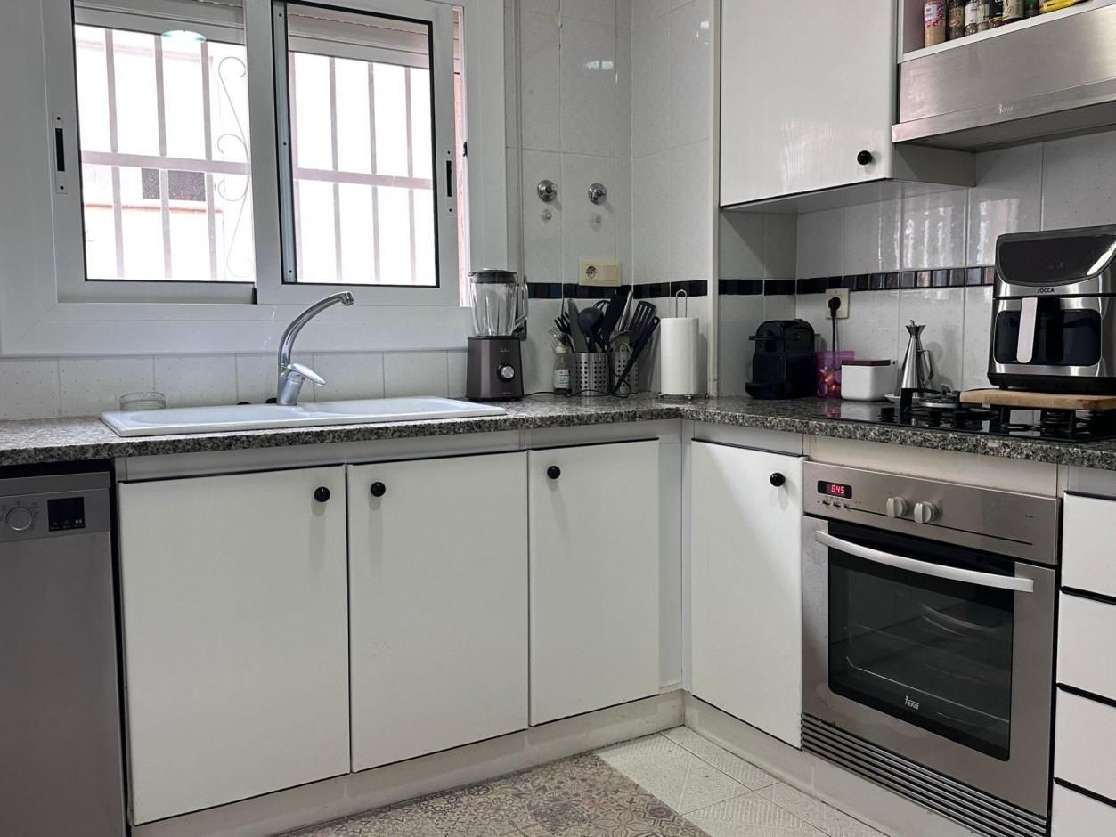 Cocina blanca con gabinetes, fregadero, electrodomésticos y una ventana.