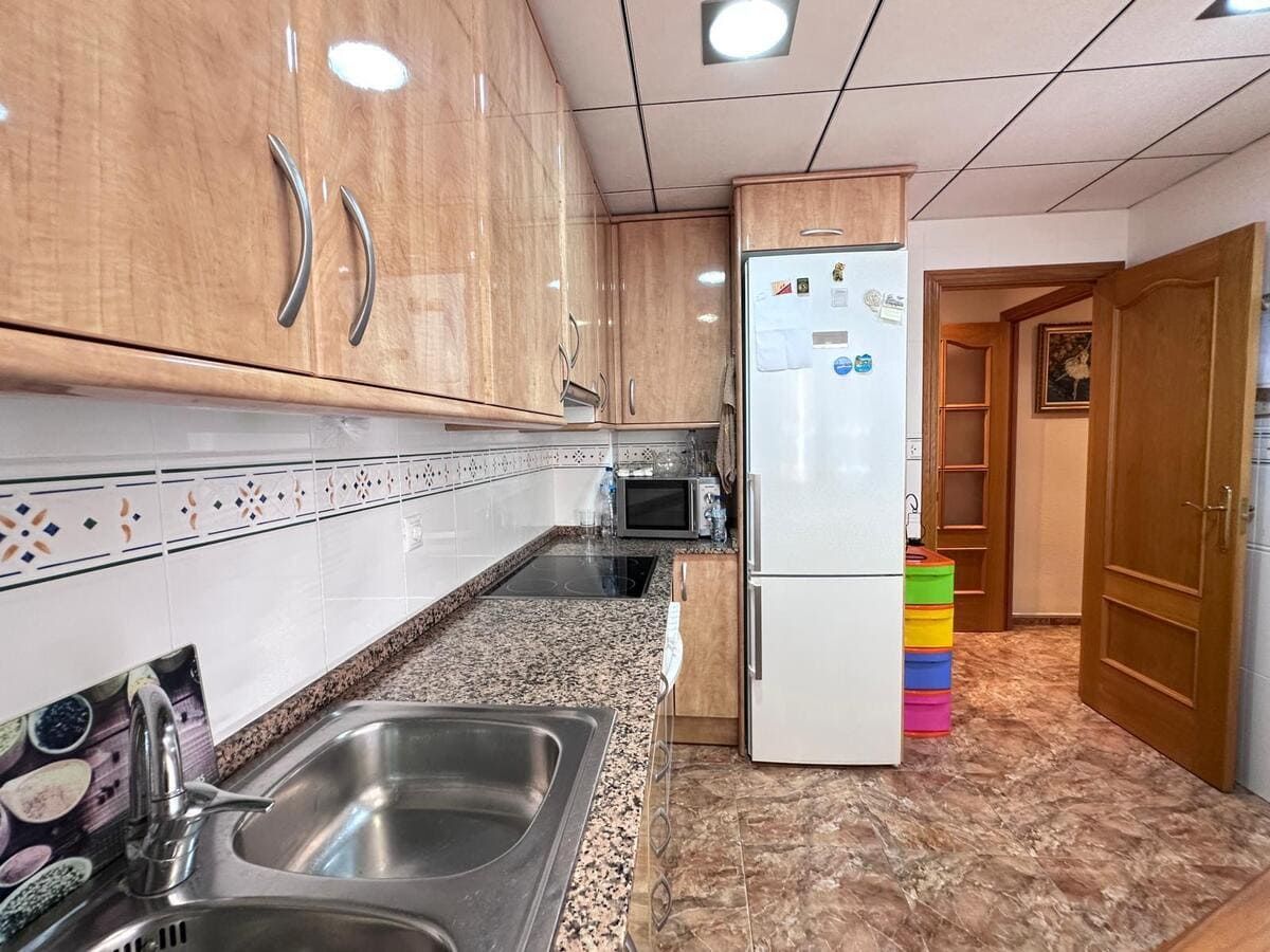 Cocina con gabinetes de madera clara, electrodomésticos de acero inoxidable y una puerta que conduce a otra habitación.