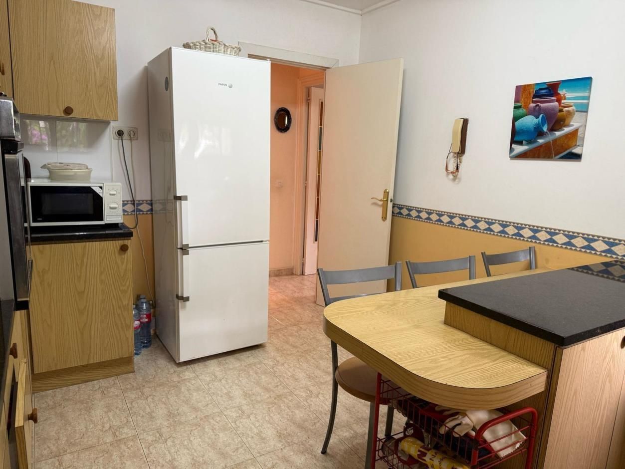 Cocina con gabinetes de madera, refrigerador blanco y una pequeña mesa de comedor.