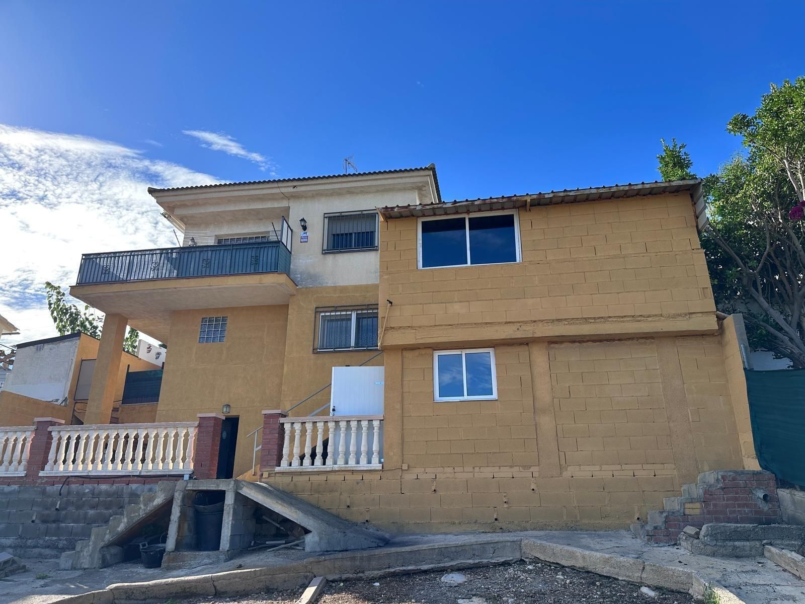 Casa amarilla de dos pisos con balcón y ventanas con marco blanco contra un cielo azul.