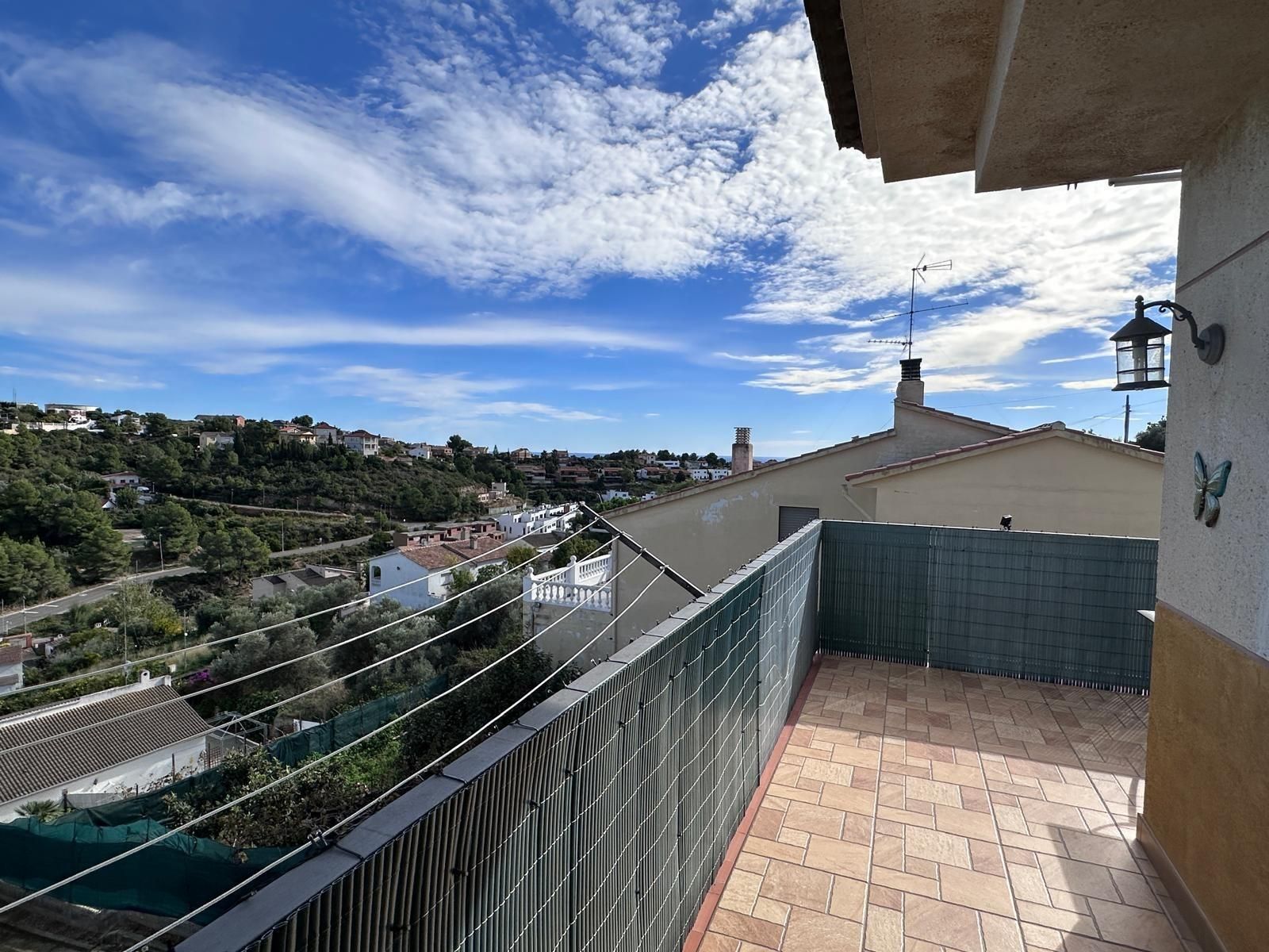 Terraza con vistas a la ciudad, cielo azul y nubes blancas. Valla verde y suelo de ladrillo claro.
