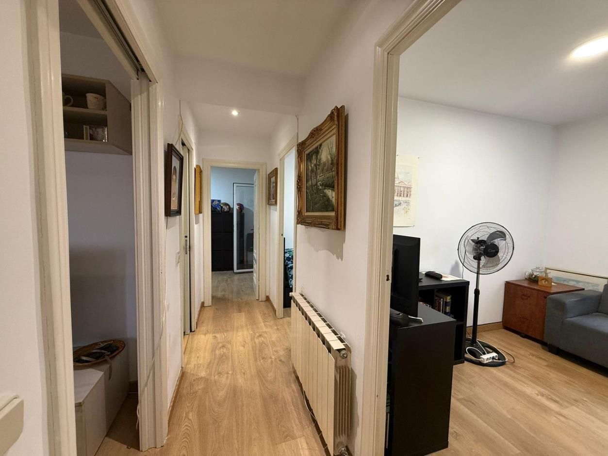 Pasillo con piso de madera, paredes blancas, puertas y obras de arte; el pasillo conduce a otras habitaciones.