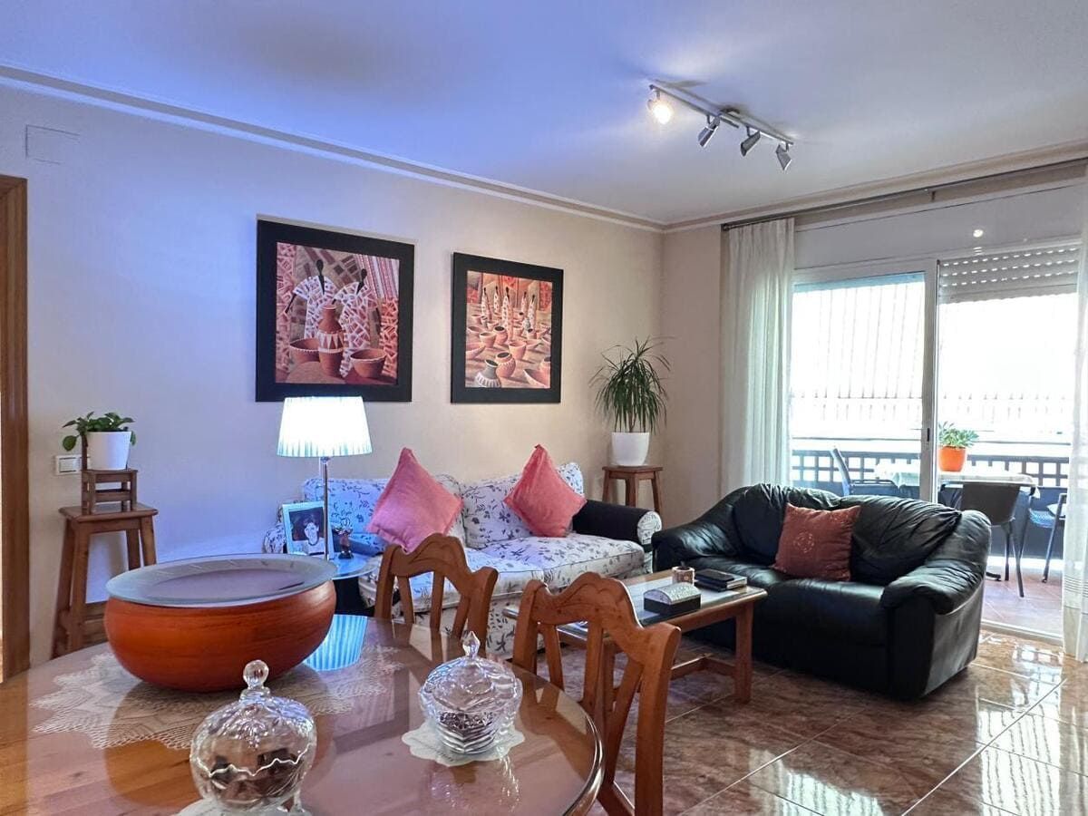 Sala de estar con mesa de comedor, sofá y balcón. Incluye obras de arte, plantas y una ventana.