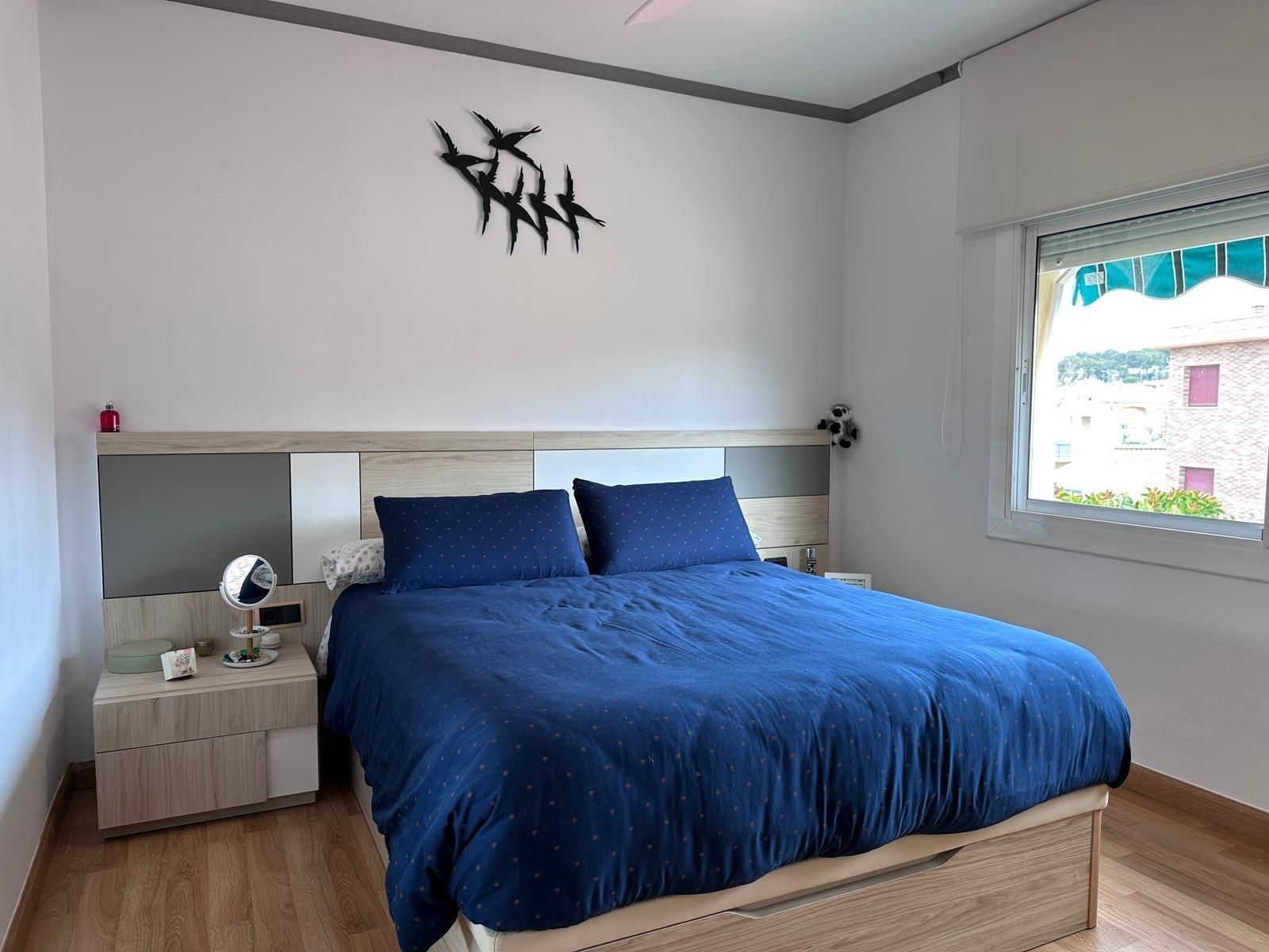 Dormitorio con cama, mesita de noche y ventana; ropa de cama azul marino, detalles de madera y decoración de pared.