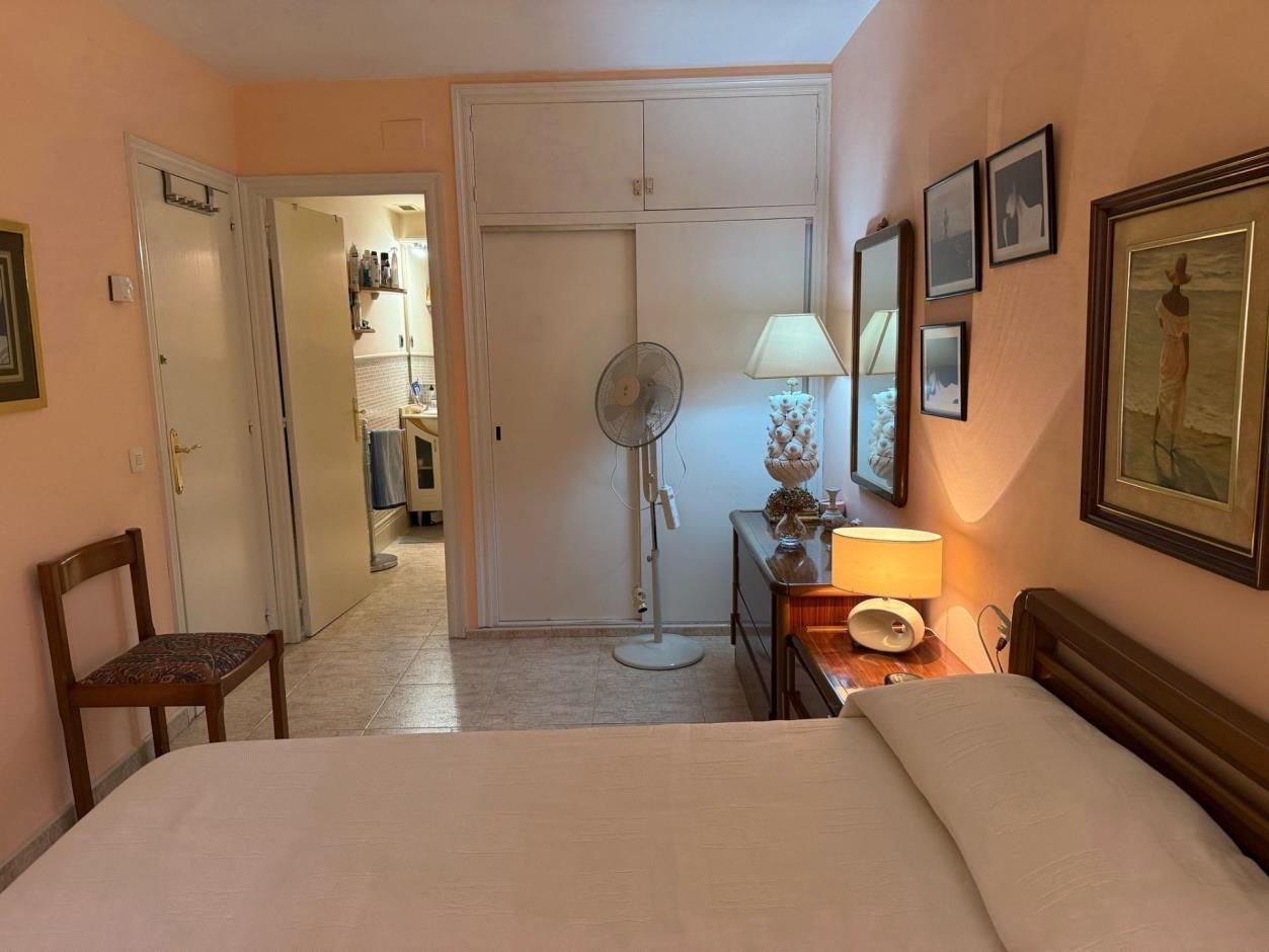 Dormitorio con cama, tocador, ventilador, obras de arte y una puerta que conduce a la cocina.