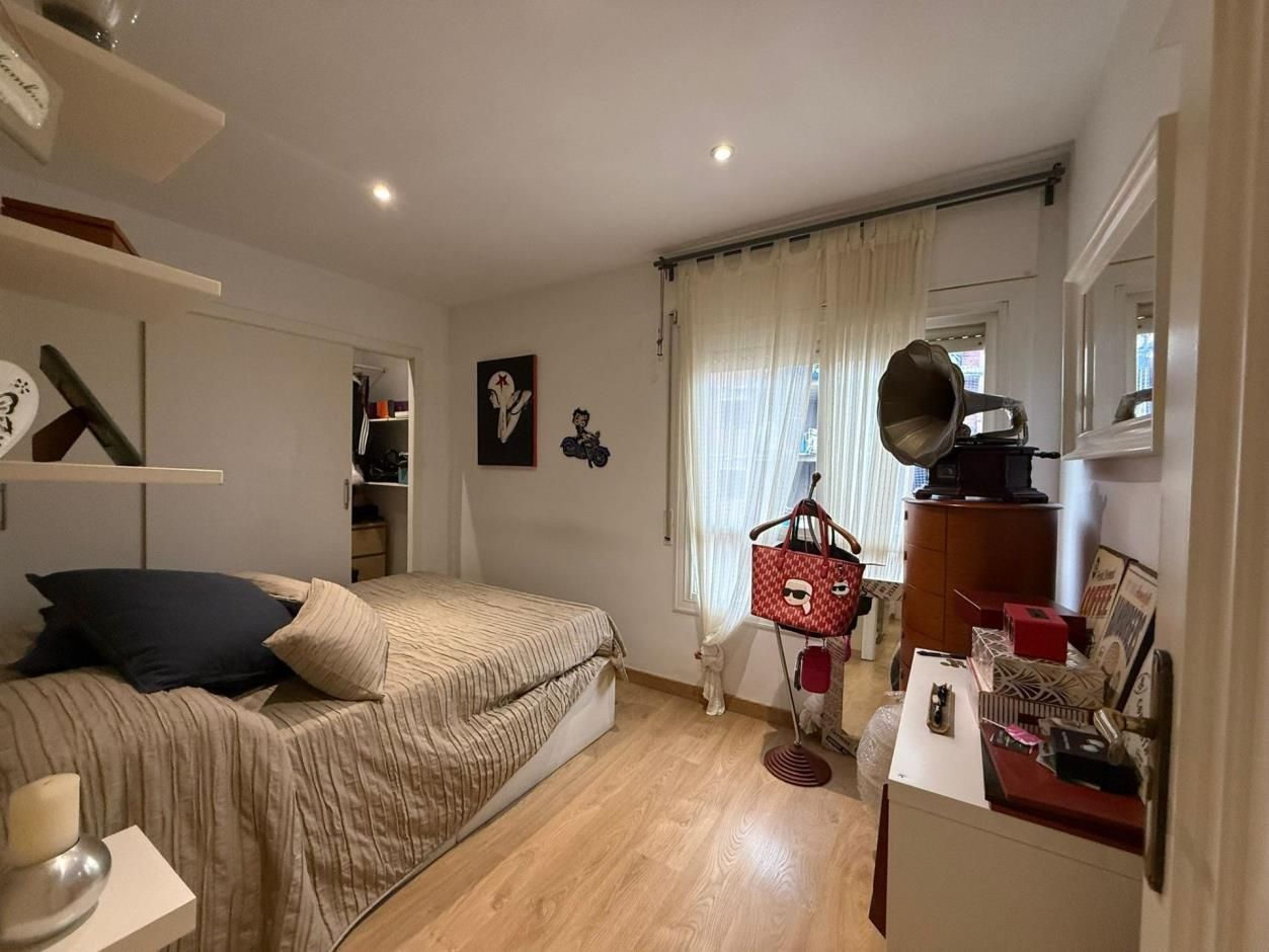 Dormitorio con cama, cortinas, fonógrafo y estanterías; suelo de madera clara y paredes blancas.