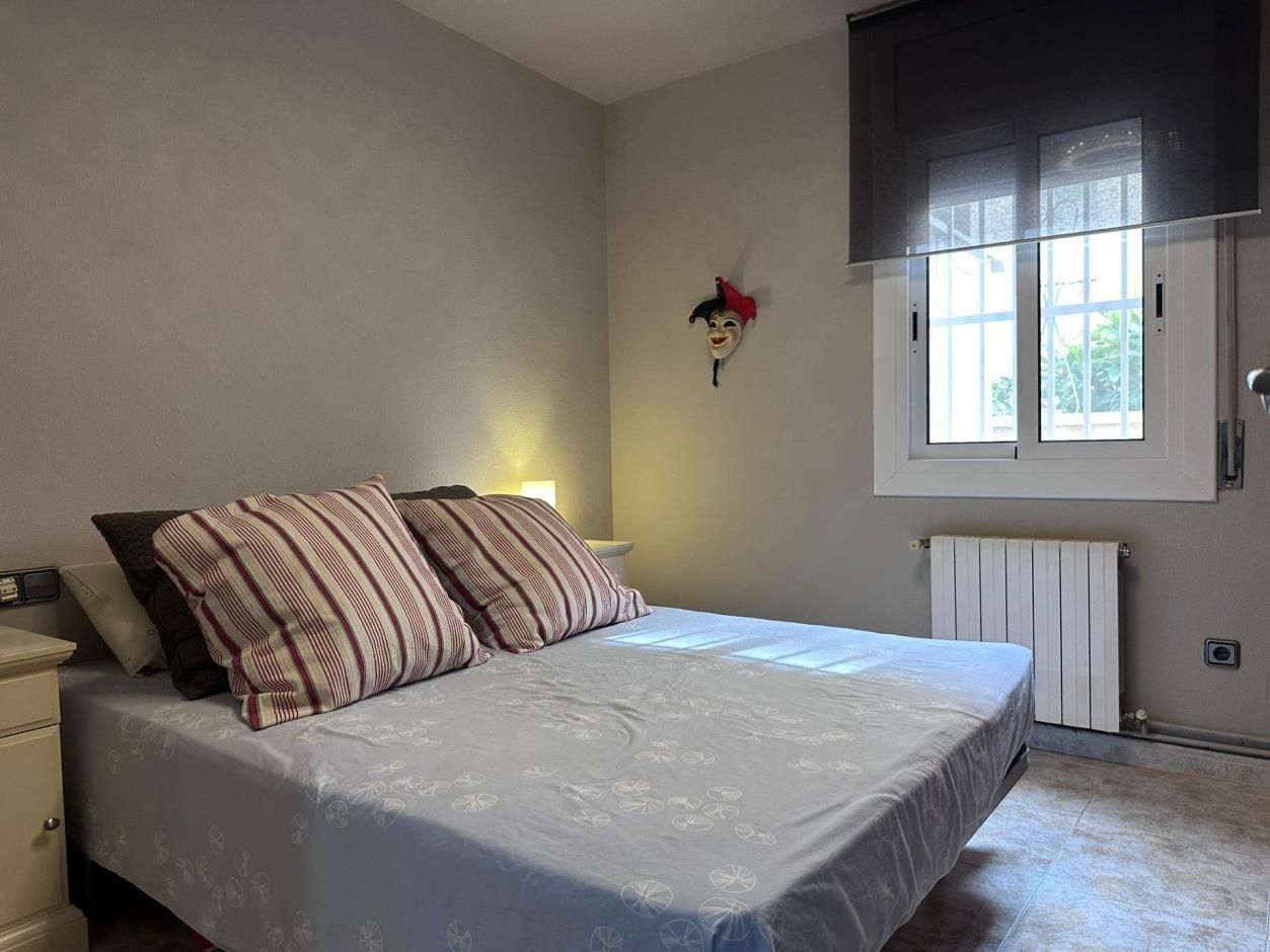 Dormitorio con cama doble, ventana y una máscara decorativa en la pared. También se ven paredes grises y una estufa.