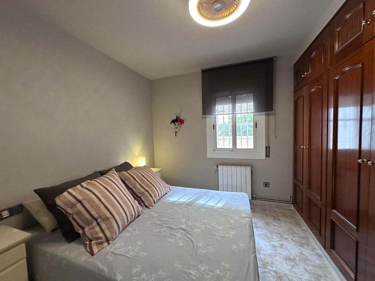 Dormitorio con cama, armario y ventana con persiana. Las paredes son de color gris claro y el armario es marrón oscuro.