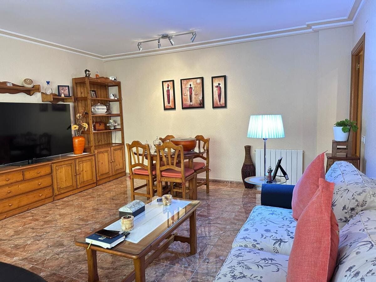 Sala de estar con muebles de madera, TV, mesa de comedor y un sofá floral.