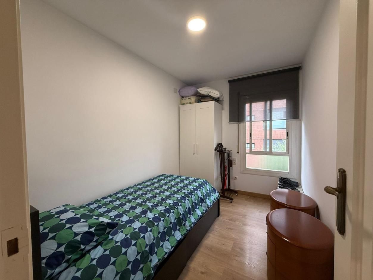 Pequeño dormitorio con una cama individual, armario y dos mesitas de noche marrones cerca de una ventana.